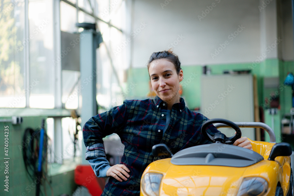 Female mechanic with hand on hip leaning on toy car in workshop Female mechanic with hand on hip leaning on toy car in workshop
