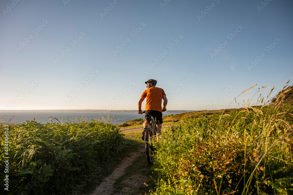 Mature male athlete riding electric mountain bike amidst plants at sunset Mature male athlete riding electric mountain bike amidst plants at sunset