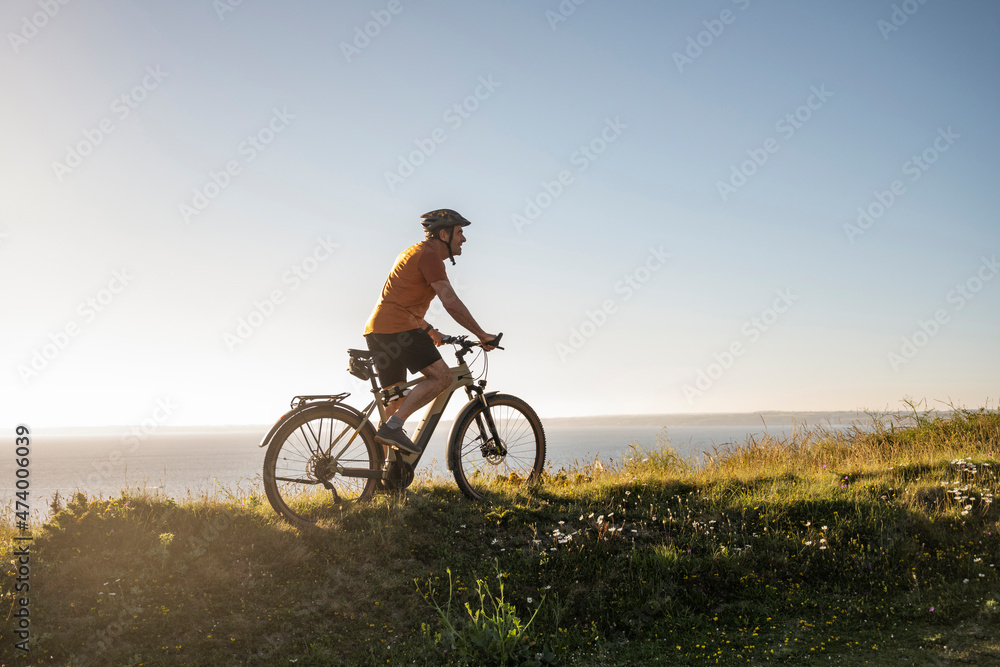 Male sportsperson riding electric mountain bike on green grass at sunset Male sportsperson riding electric mountain bike on green grass at sunset