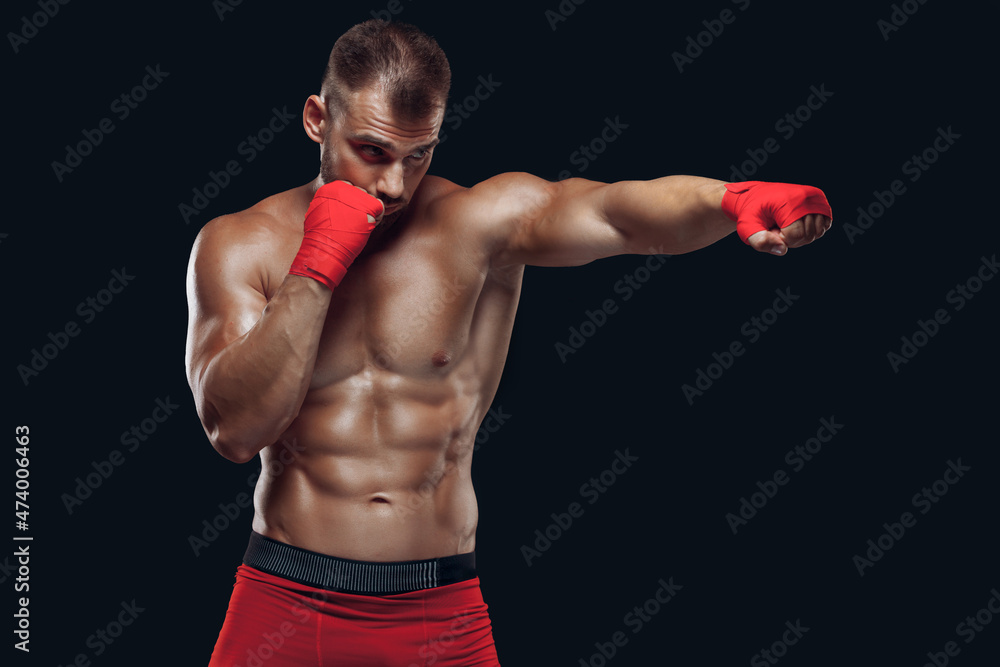 Front view of a sporty man in boxing gloves practicing fighting techniques isolated on black background