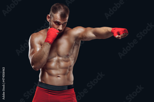 Front view of a sporty man in boxing gloves practicing fighting techniques isolated on black background