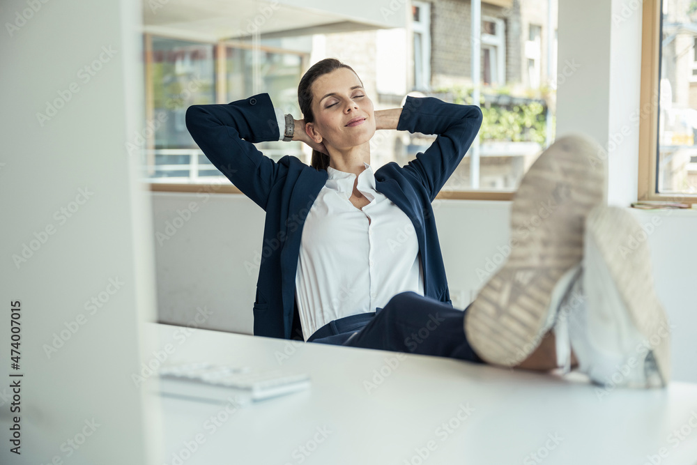 Smiling businesswoman with hands behind head relaxing in office Smiling businesswoman with hands behind head relaxing in office