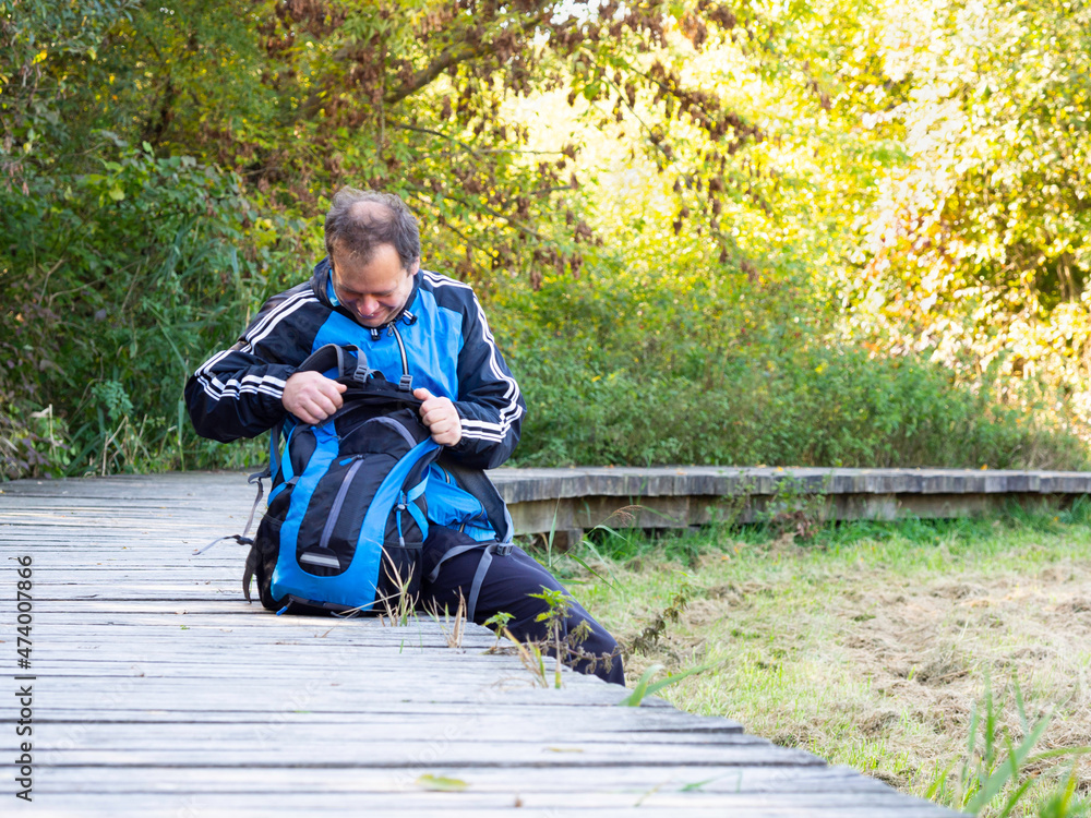 Fototapeta premium Man sitting on wooden path, middle age tourist enjoying sunny day in autumn nature