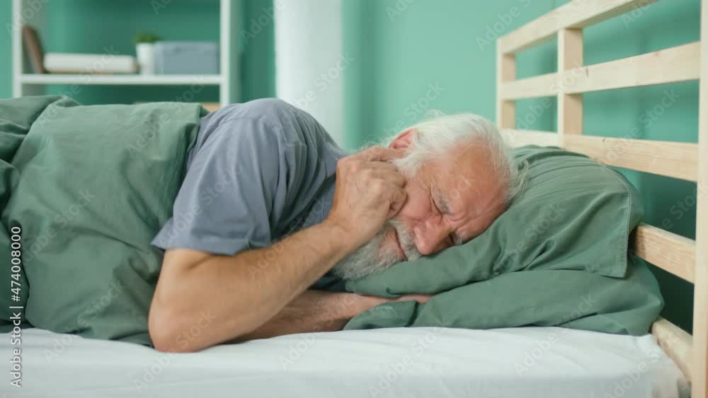 Elderly Man Tries to Rest, Gets Annoyed By Noisy Neighbors, Suffers From Insomnia on the Bed at Home. Thin Walls, Apartment Without Soundproofing, Renovation Work From Neighbors. Neighborhood Concept. Elderly Man Tries to Rest, Gets Annoyed By Noisy Neighbors, Suffers From Insomnia on the Bed at Home. Thin Walls, Apartment Without Soundproofing, Renovation Work From Neighbors. Neighborhood Concept.