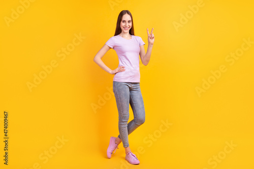 Full body photo of young cheerful girl show fingers peace cool v-symbol isolated over yellow color background © Tetiana