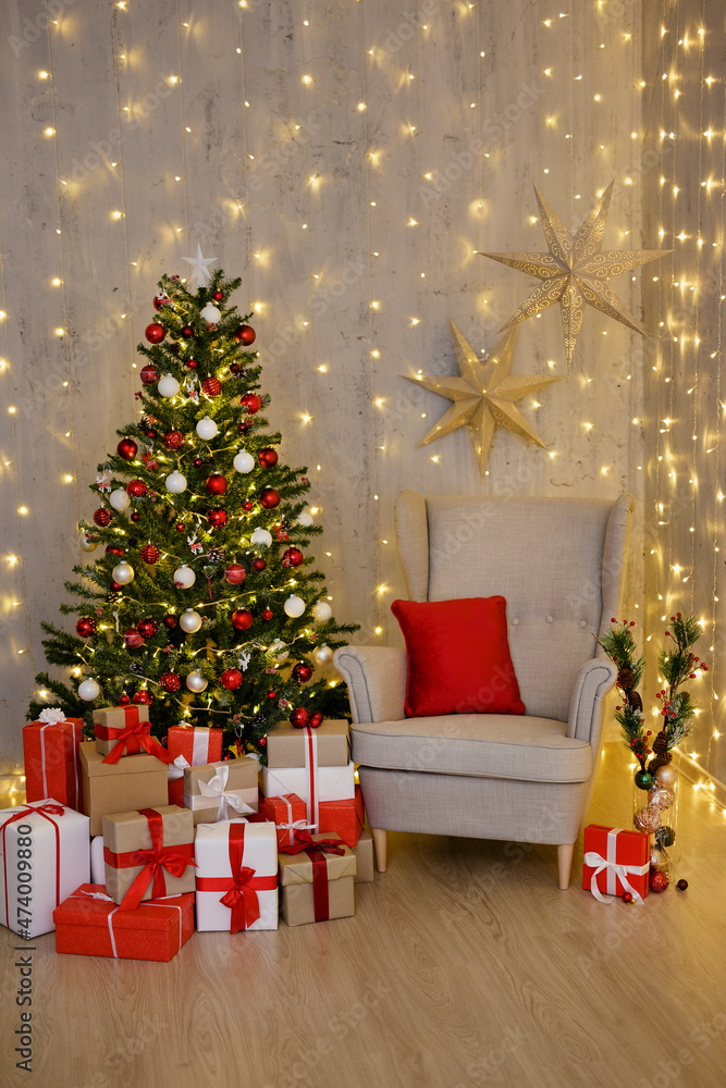 Christmas tree, heap of gift boxes, vintage armchair and Christmas decorations over grey wall with festive led lights