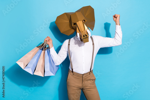 Photo of lucky funky man wear elephant mask holding shoppers rising fist isolated blue color background