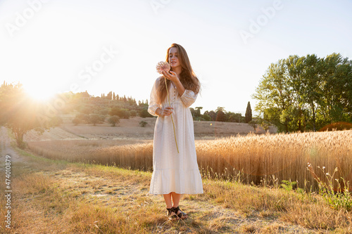 Young woman admiring garlic flower on wheat field during sunny day