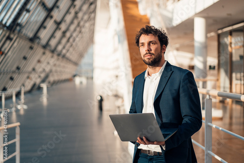 Male entrepreneur with laptop looking away while standing at office lobby