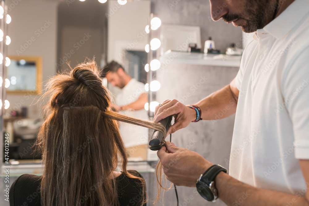 Male hairdresser using straightener on female customer's hair at salon Male hairdresser using straightener on female customer's hair at salon