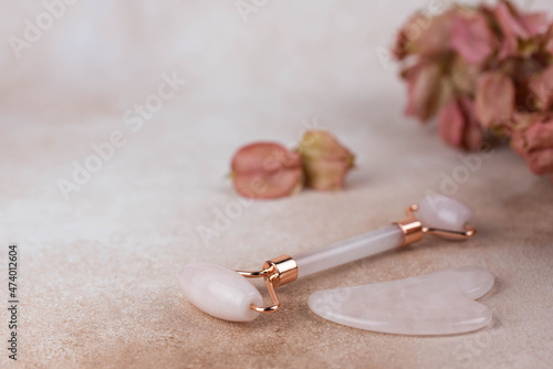 Face roller and guasha massager with dry flowers on beige background.