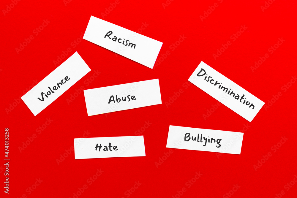 Small paper pieces with words bullying and racism, violence and abuse, hate and discrimination. Flat lay, top view on red background. Small paper pieces with words bullying and racism, violence and abuse, hate and discrimination. Flat lay, top view on red background.