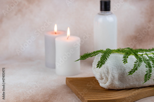 Spa still life treatment composition on massage table in wellness center. Twisted hot towel with aromatic candles on beige background. Aroma therapy setting. Concept of harmony  balance and meditation