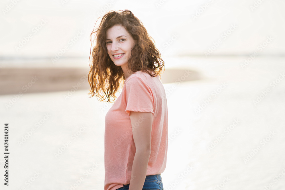 Beautiful woman looking over shoulder while standing at beach during sunny day Beautiful woman looking over shoulder while standing at beach during sunny day