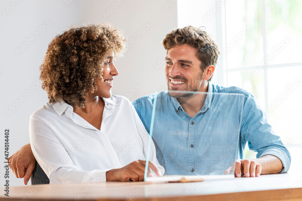 Male and female entrepreneurs smiling while sitting by futuristic glass screen at office Male and female entrepreneurs smiling while sitting by futuristic glass screen at office