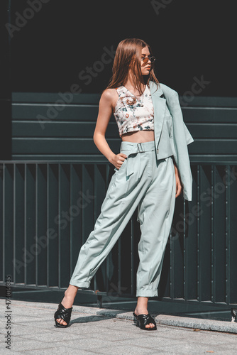 Fashion portrait of young woman wearing sunglasses, top, slingbacks, blue suit. Young beautiful happy model posing near gray metal grid photo