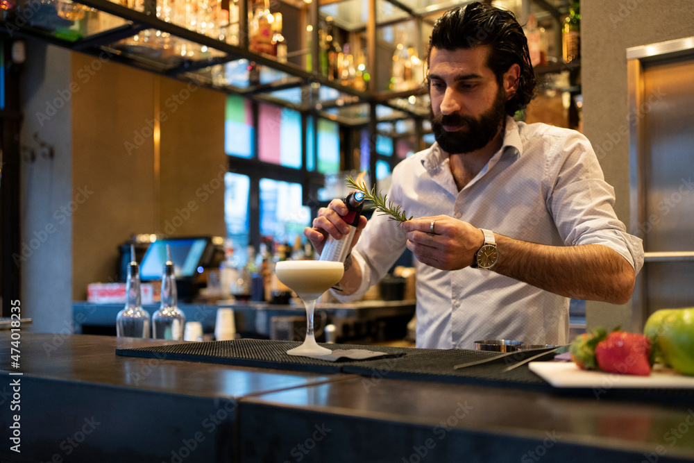 Bartender burning thyme with blow torch at bar counter Bartender burning thyme with blow torch at bar counter