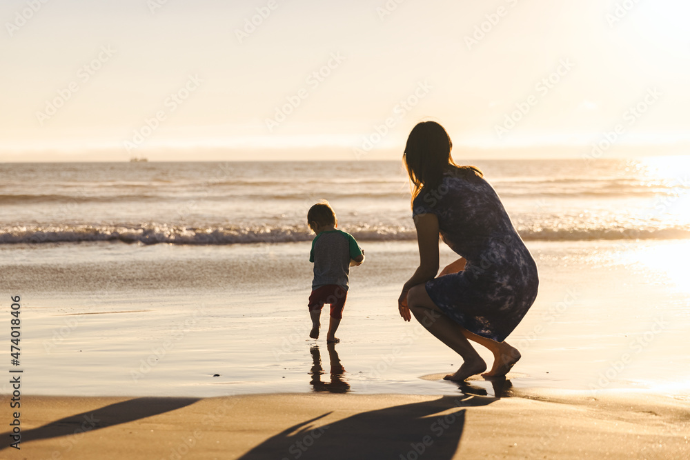 Woman Crouching Behind Son Running On Shore - obrazy, fototapety, plakaty 
