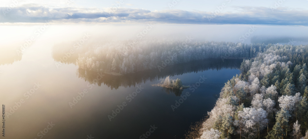 Aerial view over frozen lake in a misty forest, Finland. Winter season. View from above water surface, frozen trees and low fog clouds landscape...