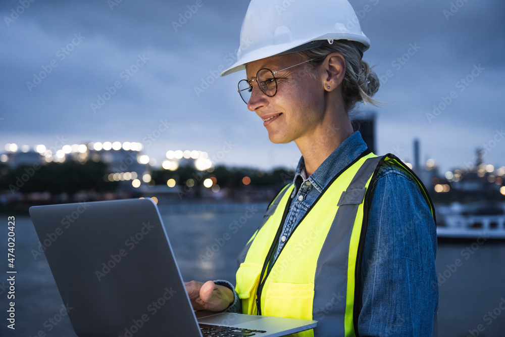 Female logistic worker using laptop at dusk Female logistic worker using laptop at dusk