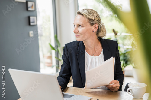 Thoughtful businesswoman with document and laptop at office photo