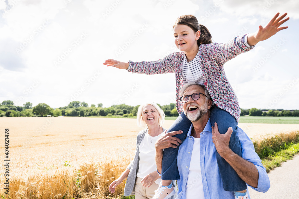 Happy man carrying granddaughter on shoulder while walking on road during sunny day Happy man carrying granddaughter on shoulder while walking on road during sunny day