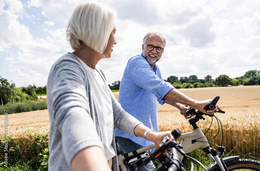 Man talking to woman while walking with bicycle on sunny day Man talking to woman while walking with bicycle on sunny day