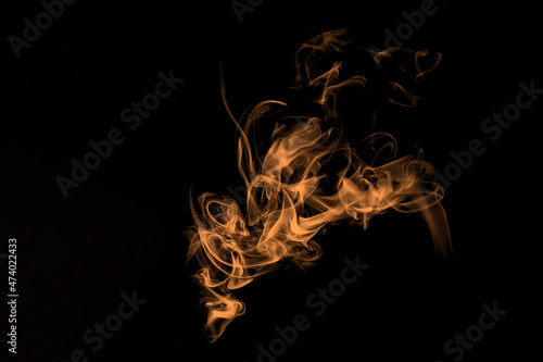 Abstract orange flame, smoke on black background. Photography of illuminated incense. Moody feeling. Dark backdrop, graphic resource for montage, overlay or texture, copy space. 