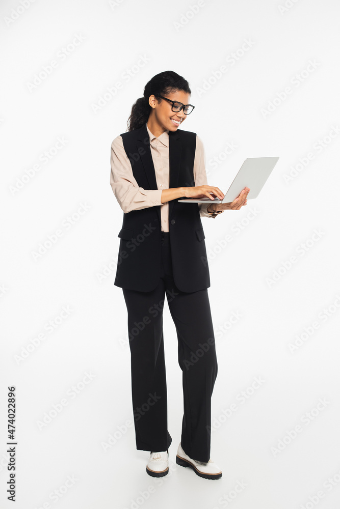 Full length of smiling african american businesswoman using laptop on white background. Full length of smiling african american businesswoman using laptop on white background.