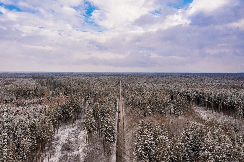 Idyllic winter panorama from an aerial view with a snow-covered forest and a to the horizon leading road.