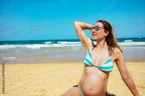 Pregnant woman close-up in sunshades sit on beach