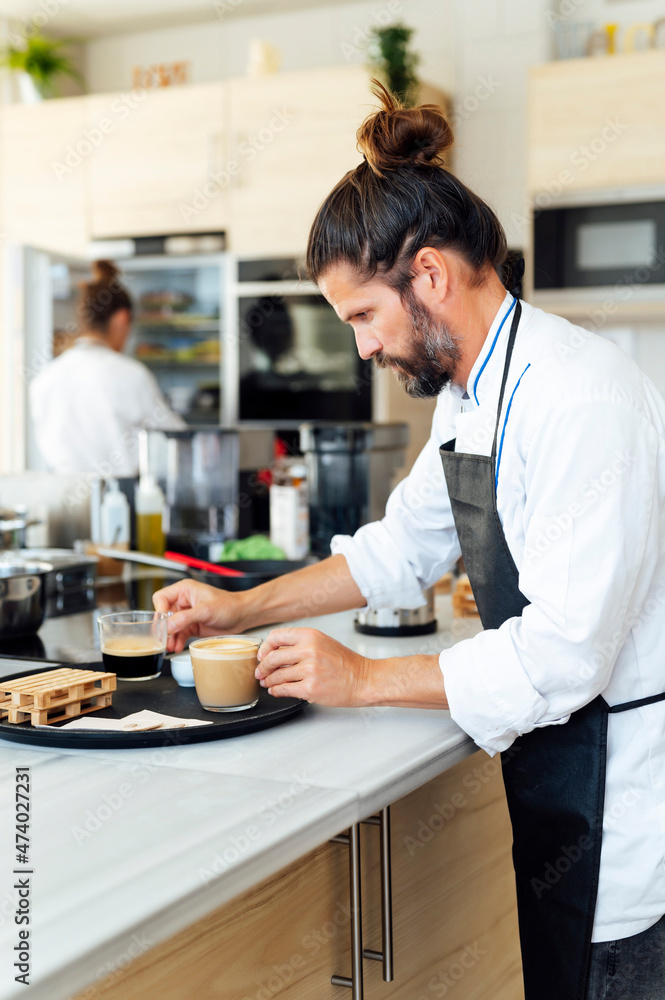 Male chef arranging coffee cups on tray in commercial kitchen Male chef arranging coffee cups on tray in commercial kitchen