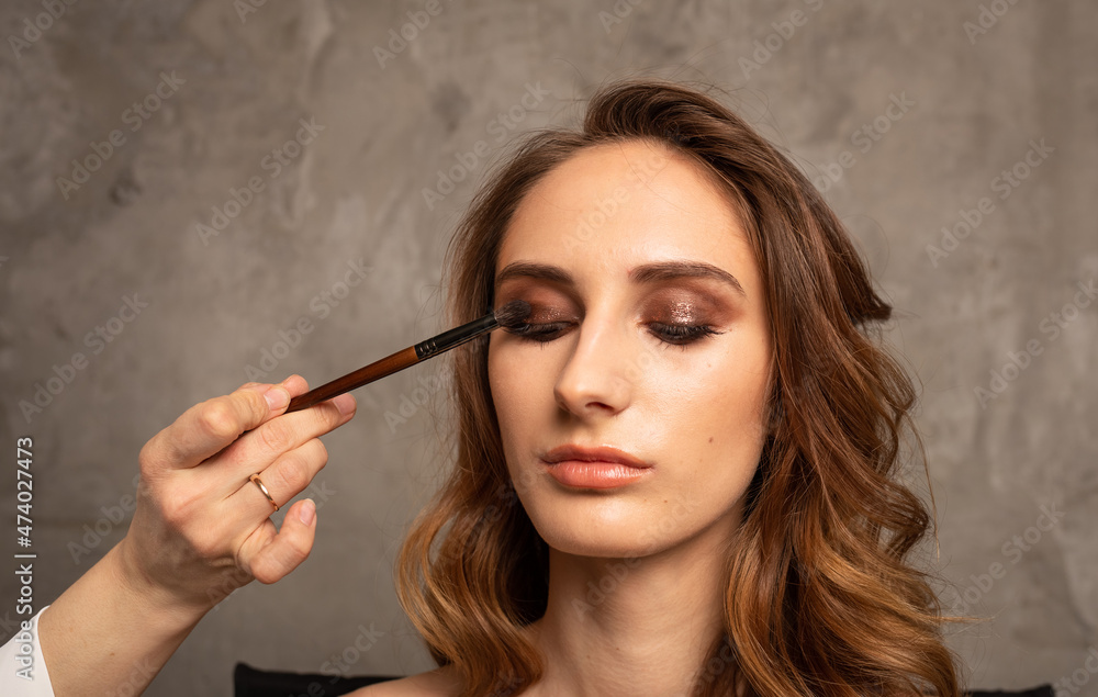 a professional makes eye makeup for a brunette girl on a gray background with a place for text. Makeup Trends a professional makes eye makeup for a brunette girl on a gray background with a place for text. Makeup Trends
