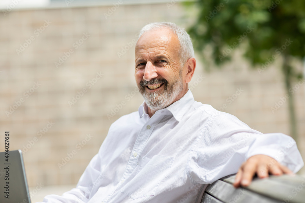Smiling businessman sitting with laptop on bench Smiling businessman sitting with laptop on bench