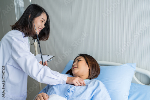Female doctor checking the health of an Asian female patient lying on the bed. At the hospital, the doctor and patient are smiling.