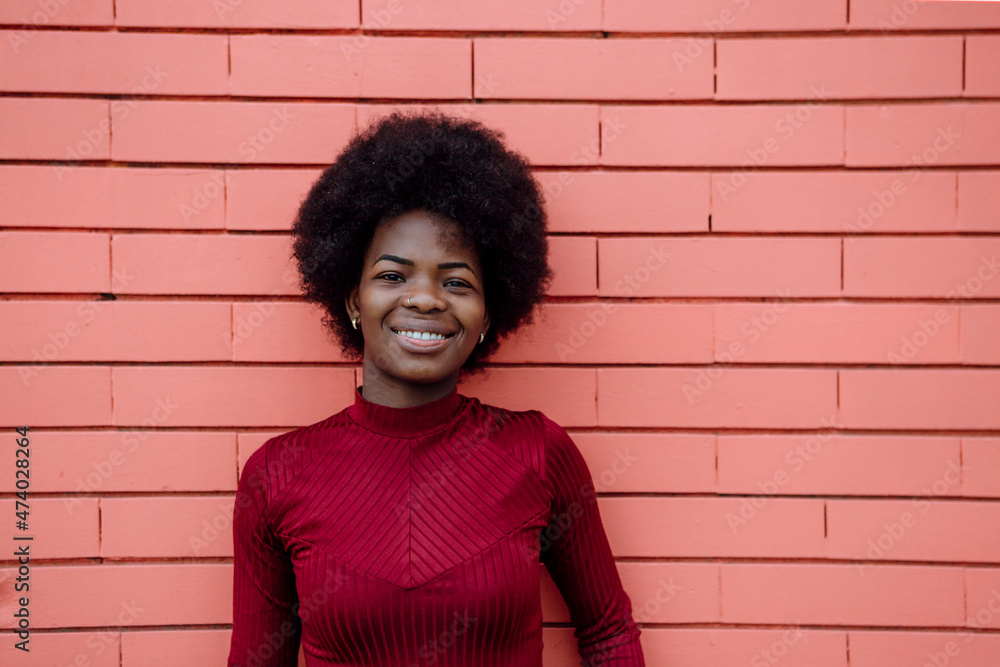 Smiling Afro woman standing in front of brick wall Smiling Afro woman standing in front of brick wall