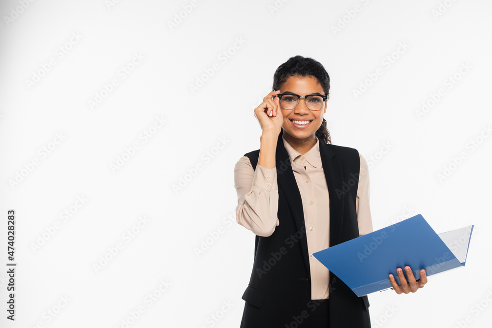 Cheerful african american businesswoman in vest holding eyeglasses and paper folder isolated on white. Cheerful african american businesswoman in vest holding eyeglasses and paper folder isolated on white.