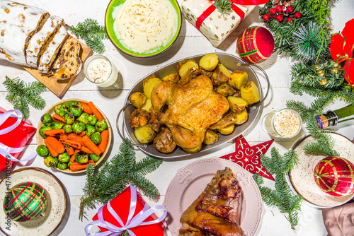 Festive Christmas dinner table with traditional foods and dished – baked ham, chicken, roasted carrots and brussels sprouts, potato, with Christmas decor and gifts 
