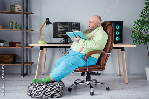 Profile side view portrait of attractive focused smart guy sitting in chair reading interesting book at office indoor work place station photo