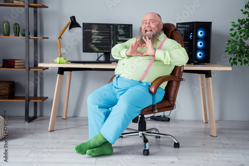 Profile side view portrait of attractive cheerful guy tech manager sitting in chair showing heart sign at office indoor workplace station photo