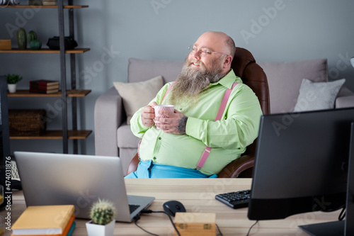 Portrait of attractive dreamy cheerful guy agent broker drinking latte work day at office indoor work place station photo