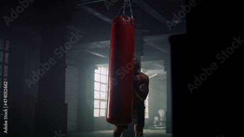 Athletic sportsman boxing punch bag in sport club. Guy training boxing in gym