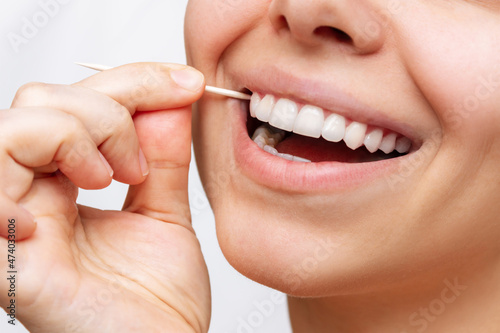 A cropped shot of a young beautiful caucasian woman brushes her teeth with a wooden toothpick after eating isolated on a white background. Oral hygiene, dental health care. Close-up. Dentistry concept photo