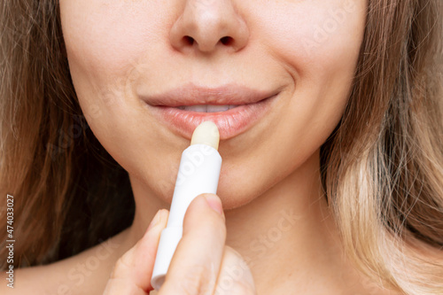 Cropped shot of a young caucasian blonde woman applying a white hygienic lipstick on her lips. Moisturizing chapstick for dry lips 