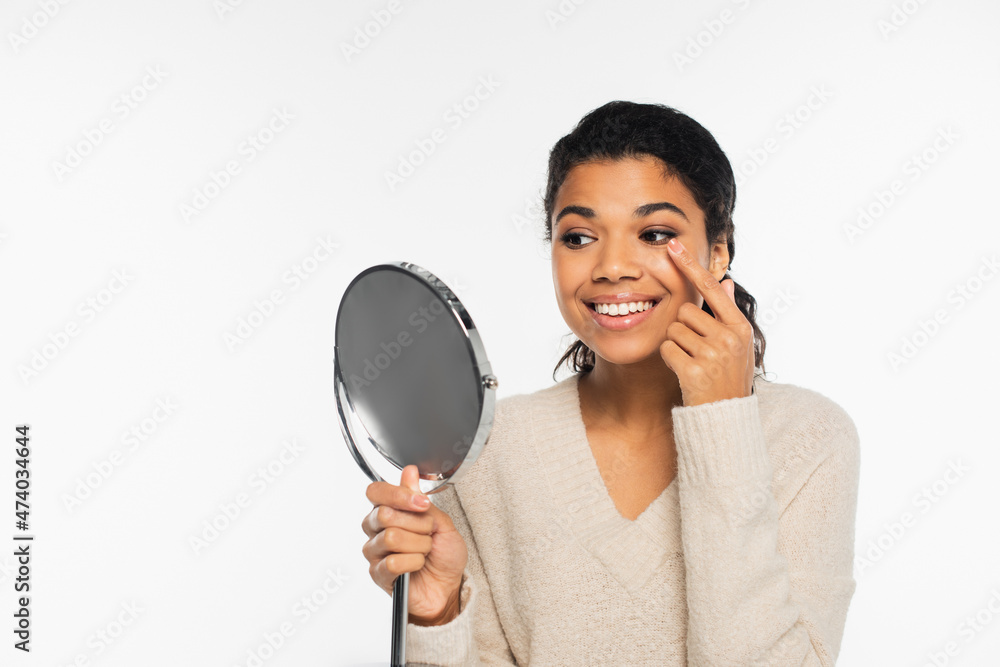 Positive african american woman wearing contact lens and holding mirror isolated on white. Positive african american woman wearing contact lens and holding mirror isolated on white.