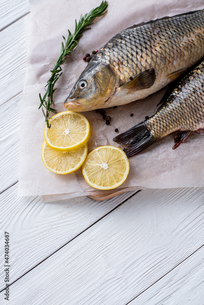 Fresh raw whole fish of mirror carp with spices, lemon and herbs on a background of parchment paper, lying on a wooden white background of boards