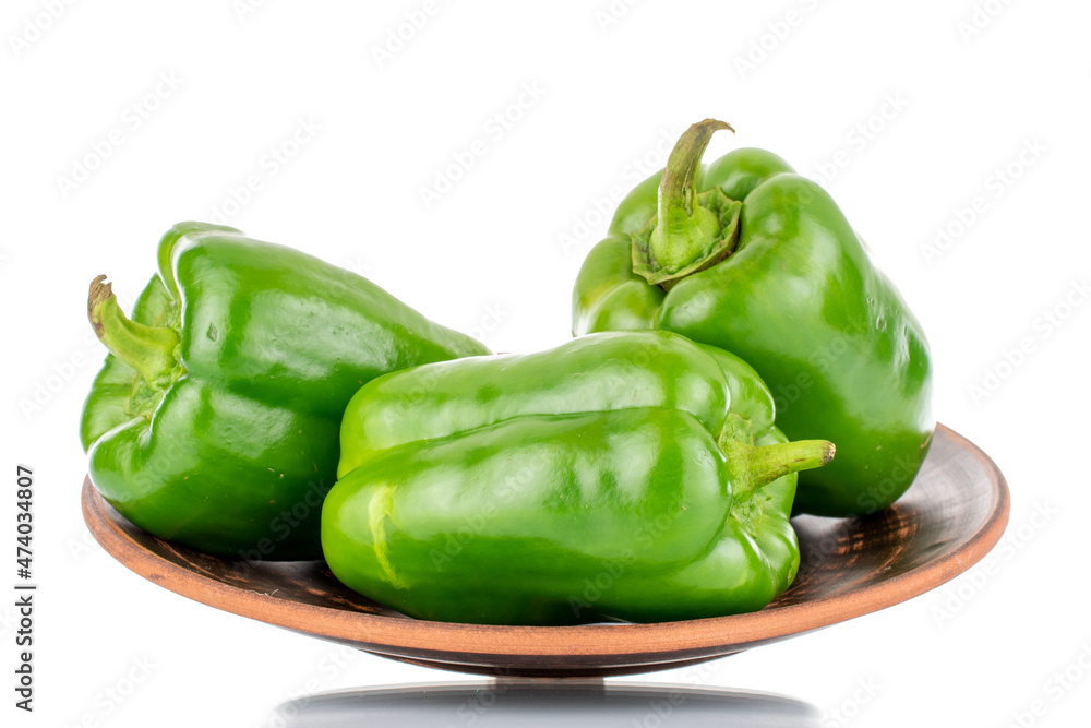Three sweet green peppers on a clay plate, close-up, isolated on white. Three sweet green peppers on a clay plate, close-up, isolated on white.
