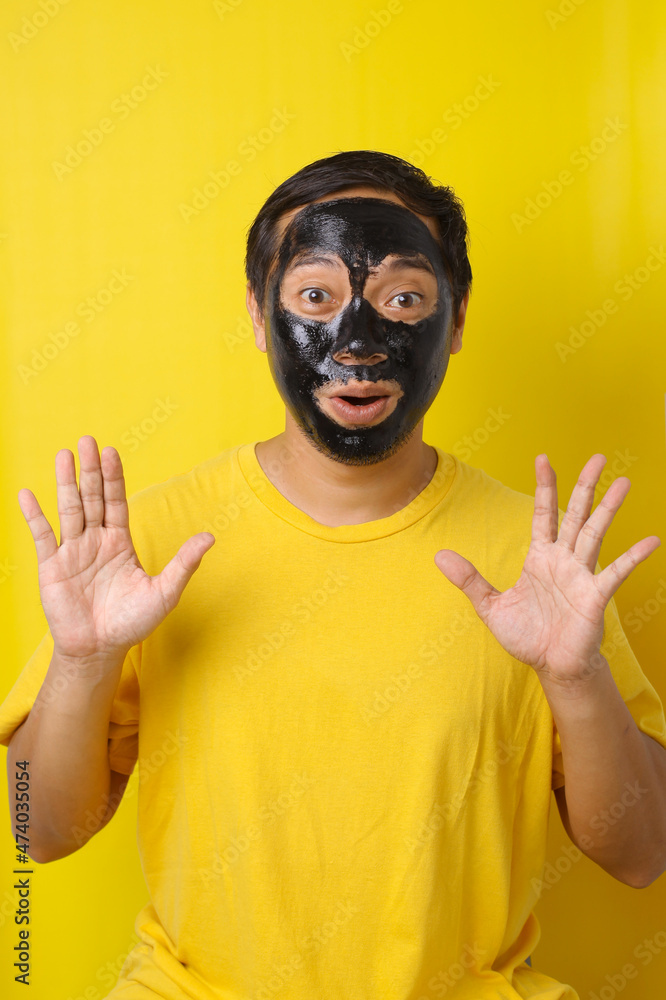 Man with cosmetics mask on the face on yellow background. Photo of man with perfect skin. Beauty and Skin care concept, funny gesture Man with cosmetics mask on the face on yellow background. Photo of man with perfect skin. Beauty and Skin care concept, funny gesture