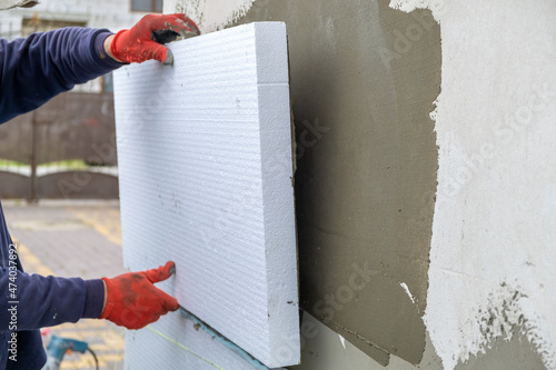 Foto Construction worker installing styrofoam insulation sheets on house facade wall