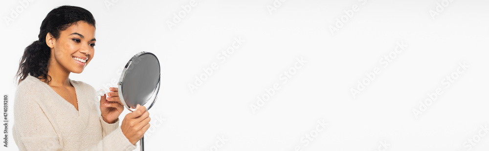 Smiling african american woman holding mirror and contact lenses isolated on white, banner. Smiling african american woman holding mirror and contact lenses isolated on white, banner.